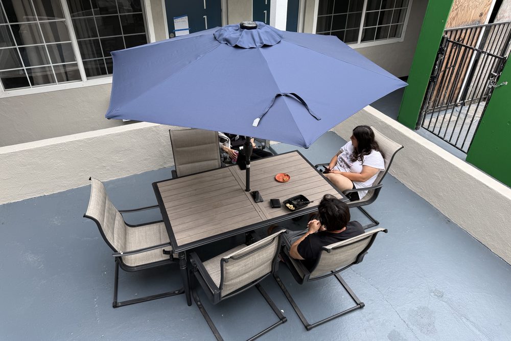 Residents sitting together at a shaded courtyard table at HarborTAY House
